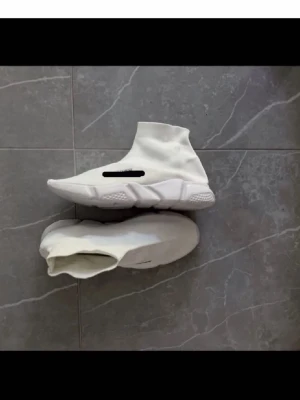 Vita Balenciaga Speed Trainer sneakers - Säljer ett par vita Balenciaga Speed Trainer sneakers med strumpliknande ovandel i stretchigt tyg och chunky sula. Minimalistisk design med Balenciaga-logga på sidan. Perfekta för dig som gillar streetwear och vill ha något bekvämt och stilrent.