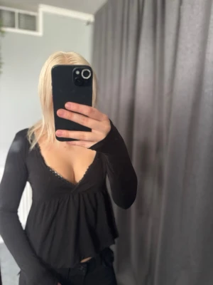 Svart långärmad topp med spets - Svart långärmad topp från 157 med djup v-ringning och spetsdetaljer längs urringningen. Modellen är flowy nedtill och har en feminin siluett som passar perfekt till jeans eller kjol.