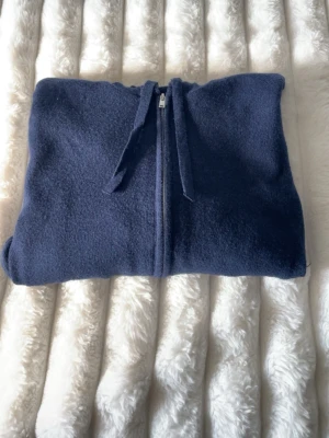 Mörkblå stickad hoodie med dragkedja - Mysig mörkblå hoodie med dragkedja framtill och justerbar huva. Tillverkad i mjukt stickat material och har ribbade muddar vid ärmslut och nederkant. Två fickor framtill för extra chill känsla. Perfekt för dig som gillar en enkel och stilren look.
