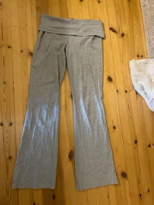 Grå bootcut leggings med låg midja - Säljer ett par ljusgrå leggings med bootcut och bred, vikbar midjeresår. Mjukt och stretchigt material som sitter skönt på kroppen. Perfekta för en avslappnad och trendig look. Passar dig som gillar bekväma men ändå snygga byxor.