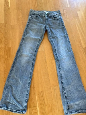 Grå bootcut jeans  - Ett par blå bootcut jeans med lätt slitna detaljer och klassisk bakficka. Jeansen har normal midja och vida ben 