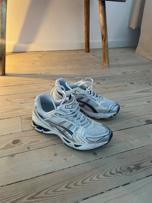 Vita Asics sneakers med meshdetaljer - Säljer ett par vita Asics sneakers med silvriga och svarta detaljer. Skorna har en sportig design med meshpaneler för bra ventilation och reflekterande inslag. Sulan är rejäl och ger bra stöd. Perfekta för dig som gillar klassiska löparskor med modern vibe.