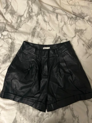 Svarta shorts i skinnimitation - Snygga svarta shorts i skinnimitation med hög midja. Snygga att styla och knappt använda, säljer då dessa har blivit för små. Dessa är från NLY trend 