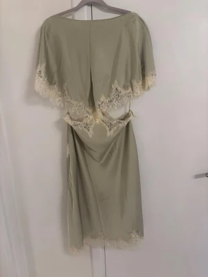 Viral zara klänning - Elegant ljusgrön långklänning i satinliknande material med vackra cremefärgade spetsdetaljer längs kanterna. Klänningen har en lös passform och draperad midja som ger en mjuk siluett. Perfekt för speciella tillfällen.