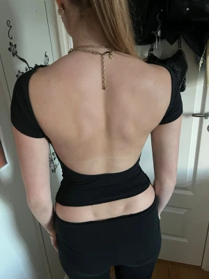 Svart topp med öppen rygg - Säljer en svart, tight topp med korta ärmar och en riktigt snygg öppen rygg. Toppen är croppad och har en enkel.Materialet känns mjukt och stretchigt, troligen polyester eller bomull.