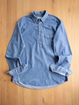 Blue Popover shirt from Eton, size L - Snygg blå popover skjorta från Eton i mjuk bomull. Skjortan har lång ärm, knappslå framtill och en bröstficka med knapp. Perfekt för en avslappnad men stilren look.