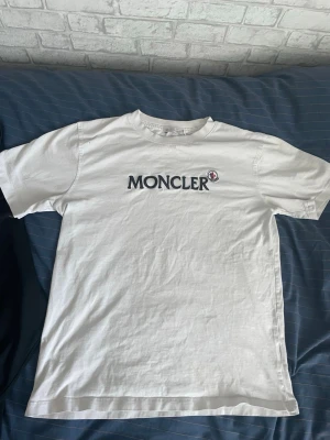 Vit t-shirt med logga - Säljer en vit t-shirt med stor broderad logga i svart och vitt på bröstet. Klassisk rund halsringning och korta ärmar. Tillverkad i mjuk bomull för en skön känsla. Perfekt för dig som gillar stilrena och exklusiva plagg. S/xs
