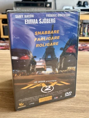 Taxi 2 – DVD – ny och inplastad - Säljer Taxi 2 (2000), den fartfyllda franska actionkomedin producerad av Luc Besson, på DVD.  Med Samy Naceri, Frédéric Diefenthal och svenska Emma Sjöberg i rollerna.  Filmen är fortfarande fabriksinplastad och oöppnad – ett fint exemplar för samlaren och för dig som gillar tidig 00-talsaction, biljakter och fysisk media. 🚕💨  Skick: Ny / oöppnad / inplastad Format: DVD Svensk utgåva: Scanbox / Boxbuster  Skickas väl emballerad.