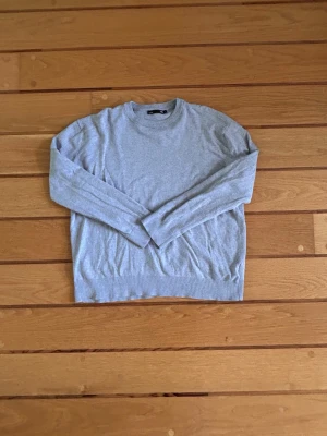 Ljusgrå stickad tröja lager 157 - Ljusgrå stickad tröja från lager 157 med rund halsringning och ribbade muddar vid ärmslut och nederkant. Tröjan har en enkel och stilren design, perfekt för lager på lager och passar till det mesta. Mjuk och skön kvalitet.