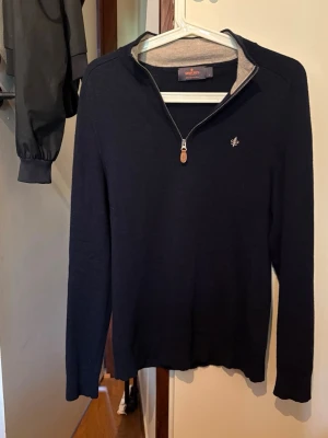 Marinblå merinoulltröja från Morris - Stilren svart tröja från Morris i 100% merinoull med halvzip och liten broderad logga på bröstet. Tröjan har ribbade muddar och en snygg kontrastfärgad insida vid kragen. Perfekt för en klassisk och avslappnad look. Väldigt bra skick skulle jag säga.