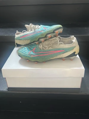 Nike Mercurial fotbollsskor turkos/guld - Säljer ett par Nike Mercurial fotbollsskor i turkos och  vita med rosa detaljer och vit sula. Skorna har en låg profil, snörning och mönstrad ovandel i syntetmaterial för bra bollkontroll. Sulan har fasta dobbar i orange för spel på konstgräs och gräs.