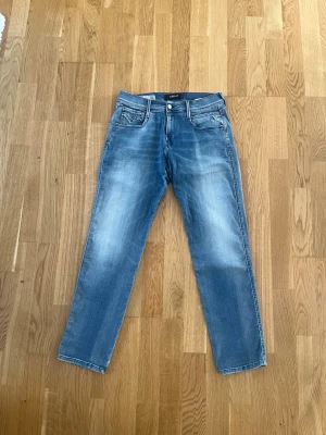 Blå jeans från Replay, W30 L30 - Säljer ett par blå jeans från Replay med klassisk femficksdesign och snygga slitningar på framsidan. Jeansen har raka ben och är tillverkade i bomull. Perfekt för dig som gillar en avslappnad och tidlös look.