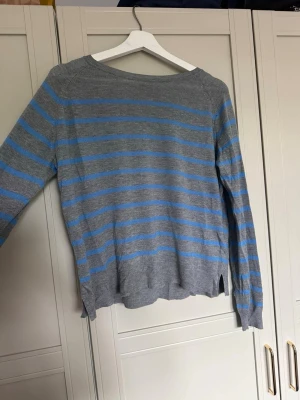 Gråblå randig stickad tröja - Stickad tröja från Zara i ljusgrått med tunna horisontella blå ränder. Tröjan har lång ärm, rund halsringning och små slitsar i nederkanten. Enkel och stilren design.