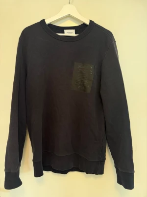 Mörkblå tröja från Dondup - Hej! Säljer en mörkblå tröja från Dondup med rund halsringning och ribbade muddar. Tröjan har en diskret patch med text på bröstet och är tillverkad i mjukt bomullsmaterial. Perfekt för en avslappnad och stilren look. | Storlek: L | Skick: 8/10 | Meddela gärna vid eventuella frågor! Mvh ResellGarms 