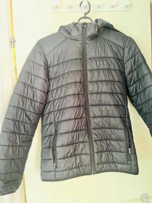 Svart dunjacka Everest - Säljer en svart pufferjacka från Everest i storlek 158/164. Jackan har huva, dragkedja framtill och två fickor med dragkedja. Tillverkad i lätt och värmande material, perfekt för kalla dagar. Snygg quiltad design och enkel att matcha med olika outfits.