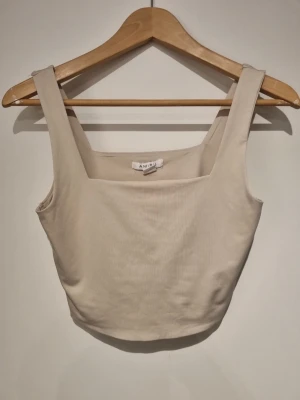 Beige ribbad linnetopp  - Snygg beige linnetopp med breda axelband och fyrkantig ringning. Toppen är ribbad och har en croppad passform som passar perfekt till höga jeans eller kjol. Enkel och stilren design som är lätt att matcha.