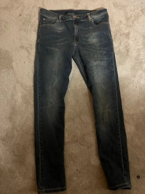Mörkblå slim fit jeans från asos  - Snygga mörkblå slim fit jeans med lätt slitna detaljer och klassisk femficksdesign. Jeansen har en smal passform och är tillverkade i denim med en något stretchig känsla för extra komfort. Perfekta för en avslappnad och trendig look.