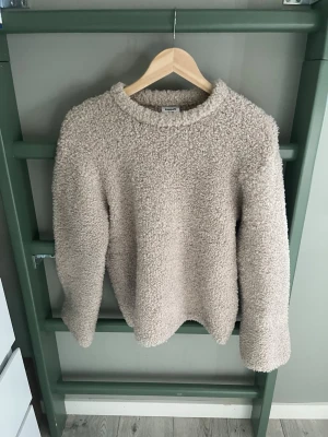 Beige fluffig stickad tröja Kappahl - Mysig beige stickad tröja från Kappahl i storlek 146/152. Tröjan har en fluffig, teddy-liknande struktur och rund halsringning. Perfekt för kalla dagar när du vill vara både varm och snygg.