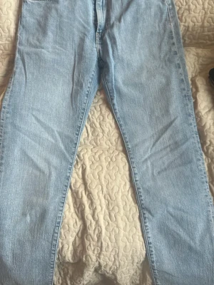 Ljusblå raka jeans från Levis (levis 502) - Säljer ett par ljusblå jeans med rak passform och klassisk femficksdesign. Jeansen har normal midja, dragkedjegylf och kopparfärgade nitar. Tillverkade i denim med en snygg tvättad look. Perfekta för en avslappnad stil.