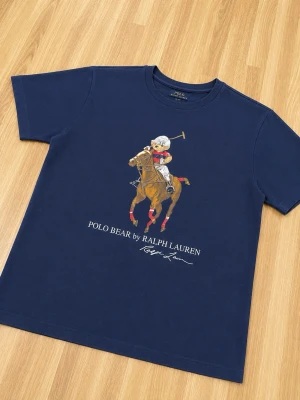 Marinblå Polo Bear t-shirt - Snygg marinblå t-shirt från Ralph Lauren med Polo Bear-tryck där björnen rider häst och spelar polo. Klassisk rund hals och korta ärmar. Trycket är detaljerat och ger en sportig vibe. Perfekt för dig som gillar streetstyle och ikoniska prints.