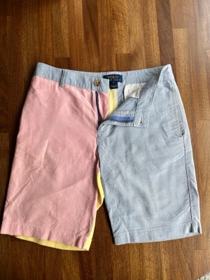 Polo Ralph Lauren patchwork shorts - Unika shorts från Polo Ralph Lauren i bomull med färgblock i ljusblått, rosa och gult. Klassisk passform med midwaist, bälteshällor, dragkedja och knappar. Perfekta för sommarens alla äventyr.