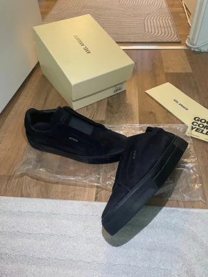 Svarta sneakers från Axel Arigato - Snygga svarta sneakers från Axel Arigato i mocka med minimalistisk design och diskret logga på sidan. Skorna har elastiska band istället för snören och en svart sula som ger en clean look. Perfekta för dig som gillar stilrena och moderna sneakers(. Obs box medföljer ej )