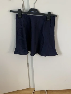 Mörkblå kortkjol från Kappahl - Snygg mörkblå kortkjol från Kappahl i en enkel och stilren design. Kjolen har en lätt utsvängd form och är tillverkad i ett mjukt material som ger en skön känsla. Perfekt att matcha med en t-shirt eller hoodie.