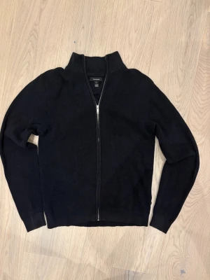 Svart stickad full-zip tröja med krage - En svart stickad tröja med hel dragkedja framtill och hög krage. Tröjan har lång ärm och en klassisk, enkel design som passar till mycket. Perfekt för lager-på-lager och snygg till jeans. Mycket sparsam användning. Grymt skick. 