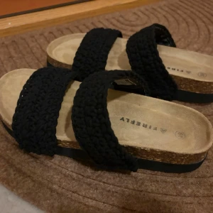 Svarta sandaler med flätade band - Snygga sandaler från Firefly med två breda, svarta flätade band över foten och bekväm korksula. Sulan är ljusbeige med svart yttersula. Perfekta för en avslappnad och trendig look. Aldrig använda utomhus och endast testats och stått i garderoben. Storlek 39 men upplever att de är lite små 