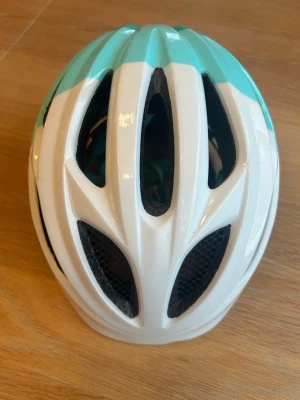 Turkosvit cykelhjälm från Occano, barn 46-51cm - Snygg cykelhjälm i turkos och vitt från Occano. Hjälmen har flera ventilationshål för bra luftflöde och en sportig design. Tillverkad i lätt plastmaterial med svart innerfoder och justerbar passform. 