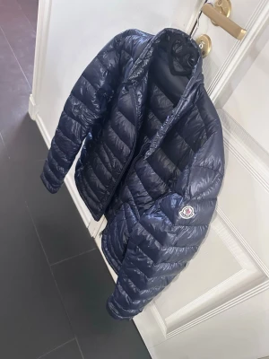 Moncler jacka - Snygg mörkblå pufferjacka från Moncler med glansig finish och klassisk quiltad design. Jackan har dragkedja framtill, två fickor med dragkedja och Moncler-logga på ärmen. Perfekt för kalla dagar och riktigt trendig stil passar M och XL skriv helst innan du köper 