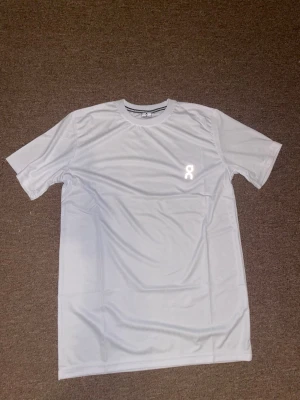 Vit sportig t-shirt från On - Säljer en vit, sportig t-shirt från On med rund hals och korta ärmar. Materialet är lätt och andas, perfekt för träning. Diskret logga på bröstet ger en clean look. Passformen är normal och tyget känns mjukt mot huden.