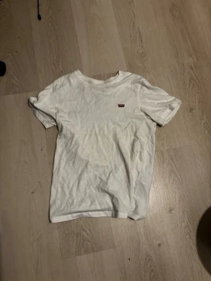 Vit t-shirt från Levi's - Klassisk vit t-shirt från Levi's med liten röd logotyp på bröstet. T-shirten har rund halsringning och korta ärmar. Tillverkad i mjuk bomull för en skön känsla och enkel stil.