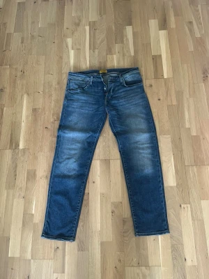 Blå jeans från Jack & Jones - Säljer ett par klassiska blå jeans från Jack & Jones med raka ben och fem fickor. Jeansen har snygga slitningar och kontrastsömmar. Perfekta till vardagslooken och tillverkade i mjukt denimtyg.