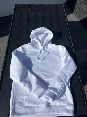 Vit hoodie från Polo Ralph Lauren - Säljer en clean vit hoodie från Polo Ralph Lauren med den klassiska broderade loggan på bröstet. Hoodien har huva med dragsko och en stor magficka. Tillverkad i mjukt bomullsmaterial som känns skönt mot huden. Perfekt för en chill och stilren look. Köpte den utomlands, ej bästa kvaliten men riktig skön, hör av er innan för mer info, ej äkta
