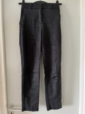 Svarta kostymbyxor från H&M - Snygga svarta kostymbyxor från H&M med raka ben och klassisk passform. Byxorna har hällor för skärp och stängs med dragkedja och knapp. Perfekta för en stilren look och passar till många olika outfits.