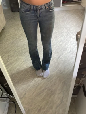 Blå bootcut jeans med låg midja - Säljer ett par klassiska blå bootcut jeans med hög midja och fem fickor. Jeansen har en snygg tvättad look och sitter tajt över låren för att sedan bli vidare nedtill. Perfekta till sneakers eller boots!