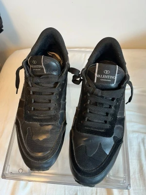 Svarta sneakers från Valentino - Snygga svarta sneakers från Valentino Garavani med coola detaljer i mocka och läder. Skorna har en klassisk låg siluett, svarta skosnören och en robust sula med mönster. Perfekta för dig som gillar stilrena och exklusiva sneakers.