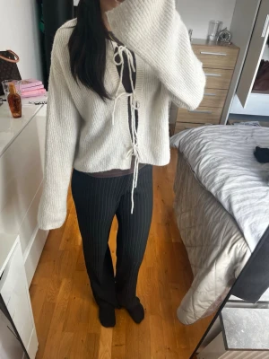 Vit stickad kofta från Gina Tricot - Säljer en superfin vit stickad kofta från Gina Tricot i ullmix. Koftan har långa ärmar, ribbstickad struktur och knytband framtill. Perfekt att slänga över en topp för en chill och trendig look.
