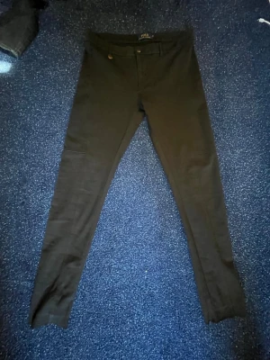 Ralph lauren chinos - Säljer ett par svarta chinos med smal passform och bälteshällor. De har bakfickor och är tillverkade i ett stretchigt material som sitter snyggt. Perfekta till en avslappnad eller uppklädd look. Perfekt för att köra golf eller bara använda