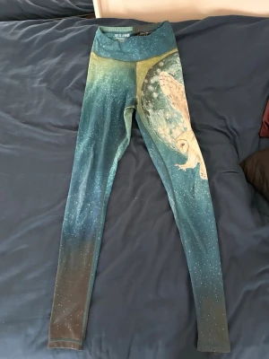Blå leggings med uggletryck - Unika leggings i blått med ett stort tryck av en uggla på ena benet. Färgen går från mörkblå till ljusare blå och har ett stjärnliknande mönster över hela tyget. Hög midja och stretchigt material som sitter skönt. Perfekta för dig som vill sticka ut med ett coolt djurmotiv. Använda men i fint skick. Storlek S. 