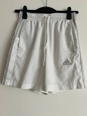Shorts adidas - Jättesnygga vita shorts från adidas. Kan användas i träning, bad eller vad man vill.   Har två fickor på varsin sida och en ficka på sidan av ena låret. Har innerbyxa med nät.   Köpt på herr avdelningen men kan även användas av dam som jag har gjort. Inköpta på stadium.   Bredd midja: ca 33-34 cm Längd: ca 44 cm