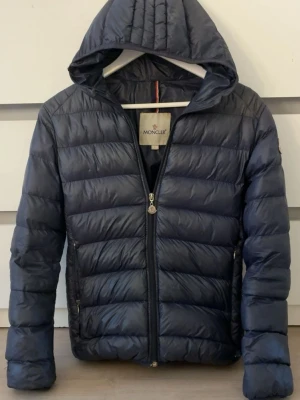 Mörkblå  Monclerjacka - Snygg mörkblå dunjacka från Moncler med huva och dragkedja framtill. ena fickan går inte att stänga, den är i storlek 1 