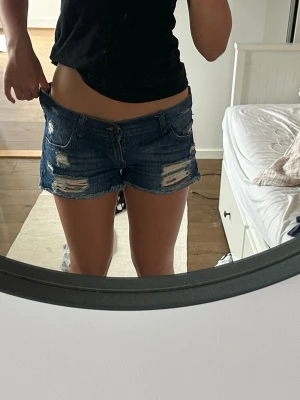 Lowrise jeansshorts - Säljer ett par blå jeansshorts med slitna detaljer. Low rise super snygga shorts!       Midja 41 cm gren 17cm