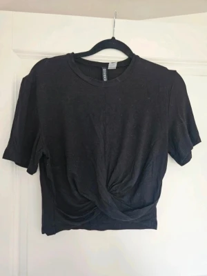 Topp H&M S - Svart topp från H&M Svart croppad topp från H&M Divided i storlek S. Toppen har korta ärmar och en snygg knytning framtill som ger en cool twist. Tillverkad i mjuk bomull, perfekt för att styla med jeans eller kjol. Enkel och stilren design som funkar till många looks.  Kan även hämtas I Partille  E1