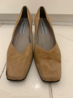 Beige mockapumps från Roberto Vianni - Snygga pumps i beige mocka från Roberto Vianni. Skorna har en fyrkantig tå och låg klack, vilket ger en trendig och stilren look. Perfekta för dig som gillar klassiska men moderna detaljer. Materialet är mjukt och ger en exklusiv känsla.