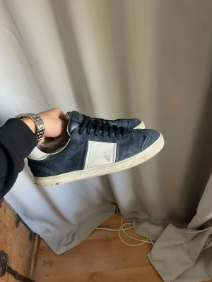 Mörkblå Valentino Flycrew  - Snygga mörkblå sneakers i mocka från valentino med vita detaljer på sidan och vit sula. Klassisk låg modell med svarta skosnören och diskret logga på sidan. Perfekta för en stilren och avslappnad look.