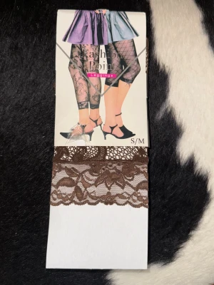 Bruna spetsleggings S/M - Säljer ett par bruna capri tights i spets med blommönster. De är stretchiga och har en kortare caprilängd som slutar under knät. Perfekta för dig som vill ha en unik och trendig look med snygga detaljer.