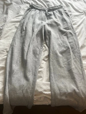 Grå mjukisbyxor  - Ett par klassiska grå mjukisbyxor med resår i midjan och dragsko för skön passform. Byxorna har raka ben och sidofickor. Tillverkade i mjukt sweatshirtmaterial som är perfekt för chill dagar hemma eller när du vill vara bekväm. Dom har en liten fläck med nagellack som spillts så därför säljer jag dom för billigare. 