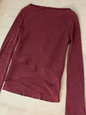 Vinröd ribbad tröja  - Säljer en vinröd långärmad tröja med ribbad struktur och snygg asymmetrisk nederkant. Tröjan är använd få gånger och säljer för jag har för mycket kläder